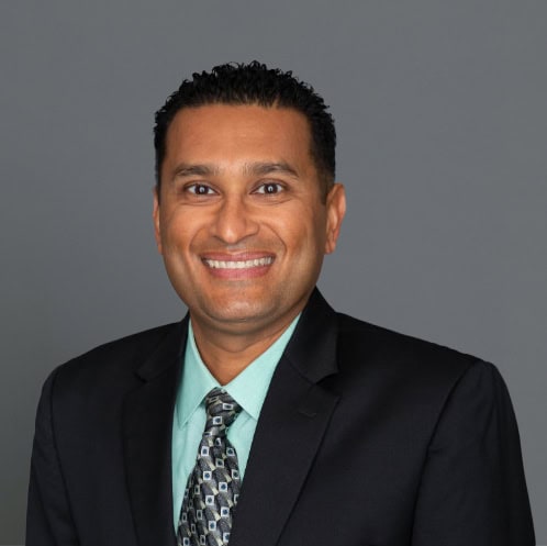 Headshot of Ravi Patel, M.D. in professional wear with a grey background.
