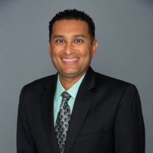 Headshot of Ravi Patel, M.D. in professional wear with a grey background.