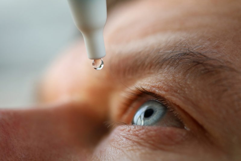 eye drops falling in to open blue eye close up